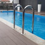 Escada de piscina em aço inoxidável junto a água azul cristalina com rebordo em pedra clara