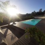 Piscina com água cristalina rodeada por chão em madeira escura ao pôr do sol