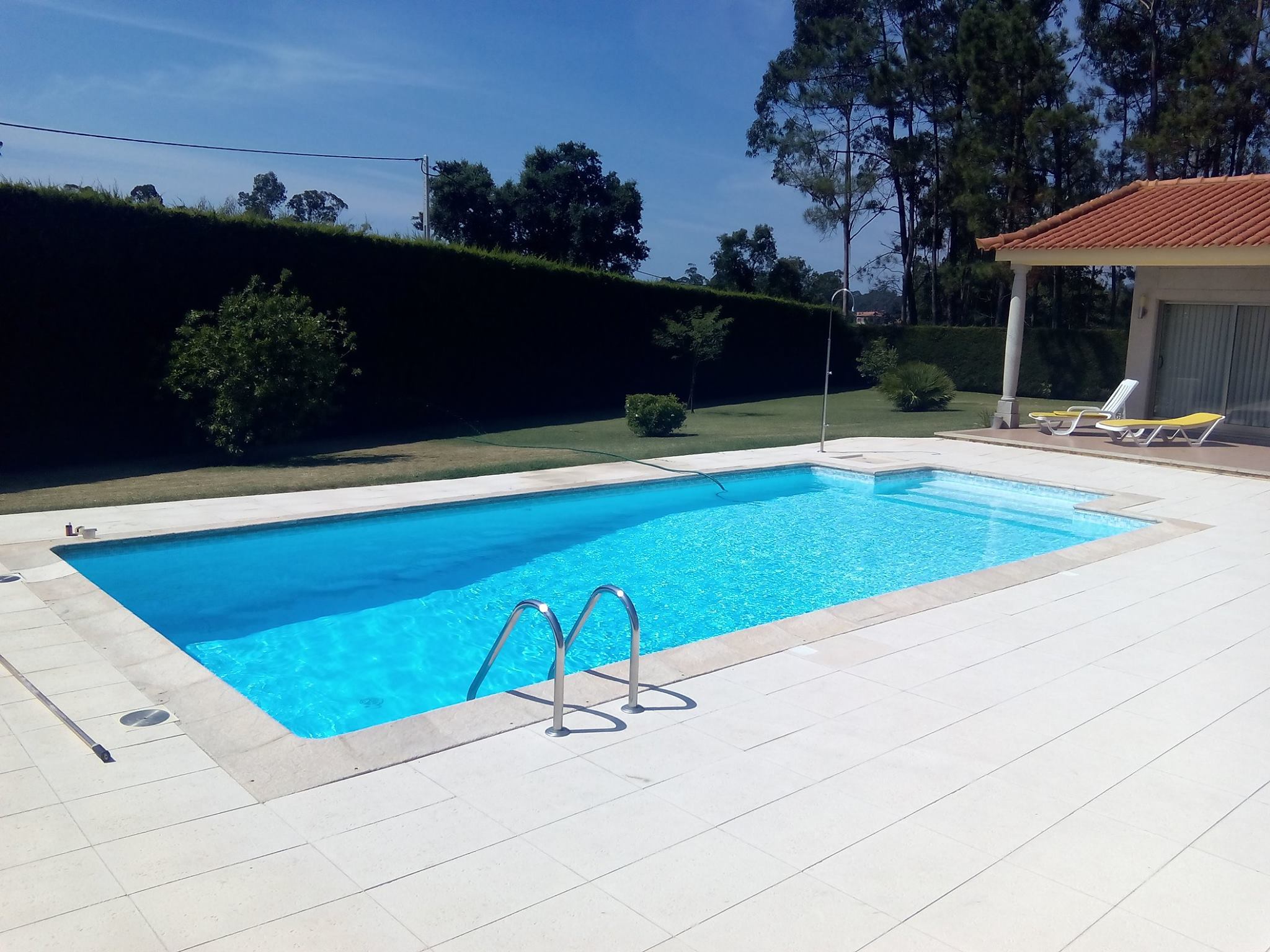 Piscina com água azul cristalina num dia soalheiro, com um enorme ambiente de verão